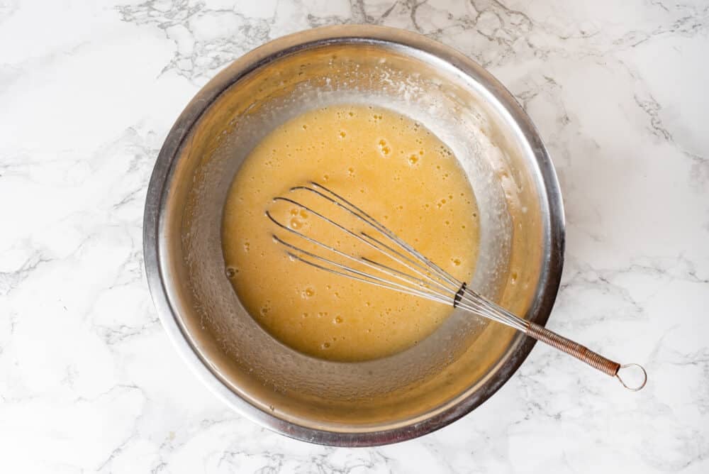 Butter added to eggs and sugar in a bowl with a whisk.