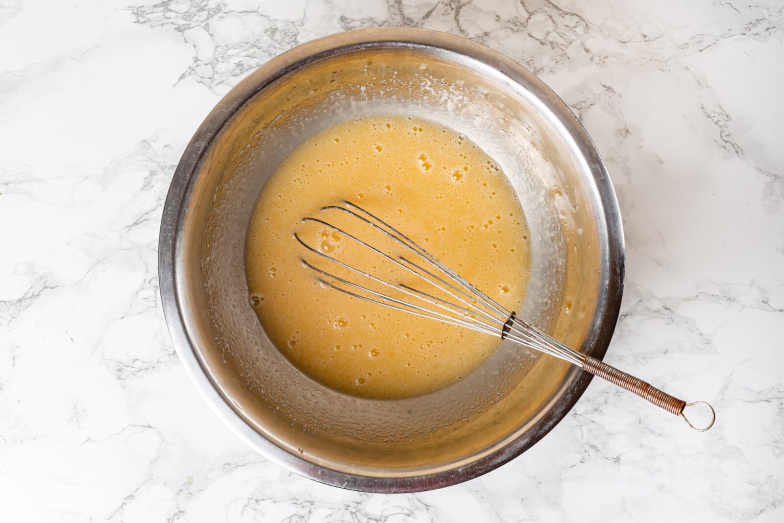 Butter added to eggs and sugar in a bowl with a whisk.