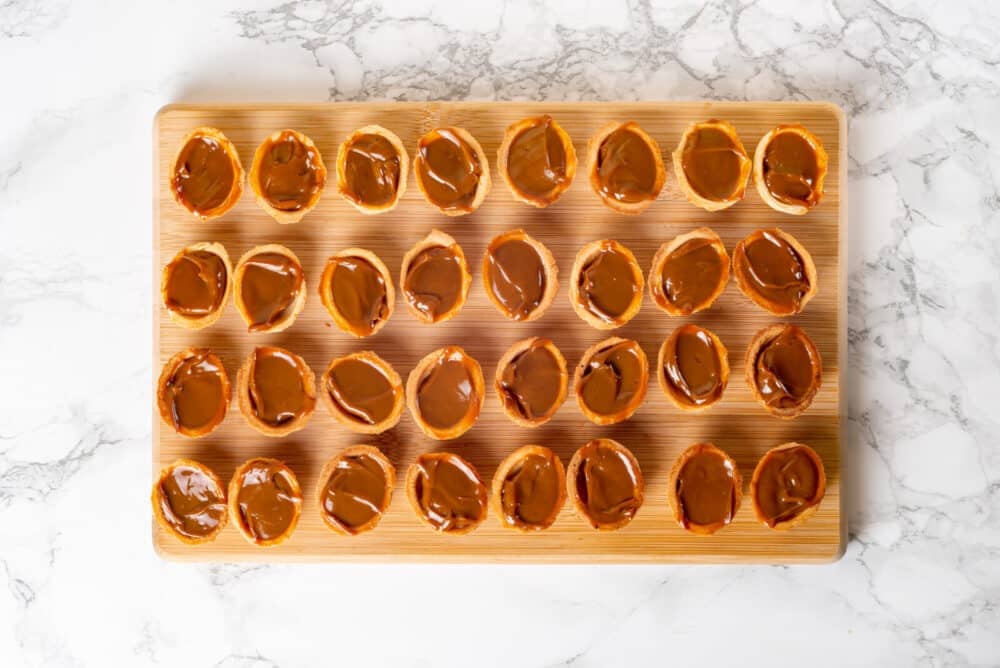 Filling walnut cookie shells with dulce de leche filling on a wooden board.