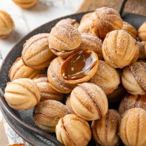 Walnut cookie halves open showing inside dulce de leche filling atop a stack of more walnut cookies covered in powdered sugar.