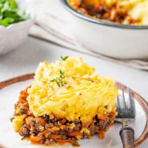 shepherds pie with lamb on a white plate with a brown rim and a fork.