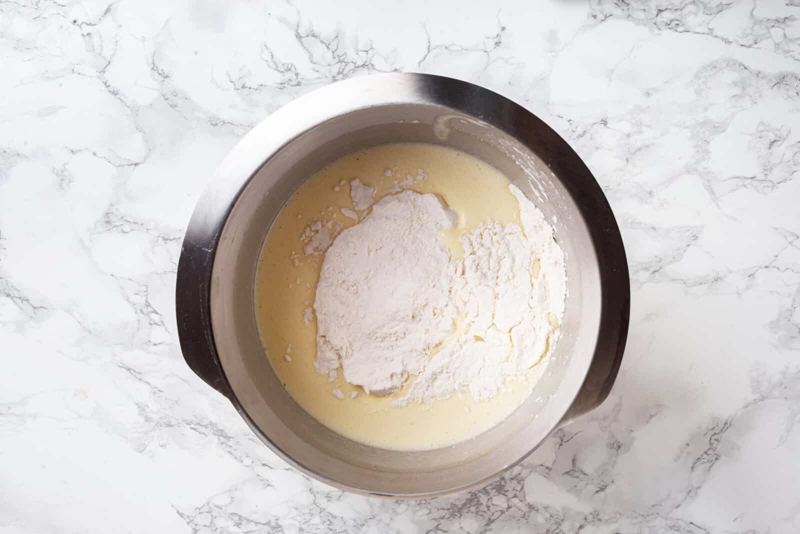 Added dry ingredients into wet ingredients in a silver bowl.