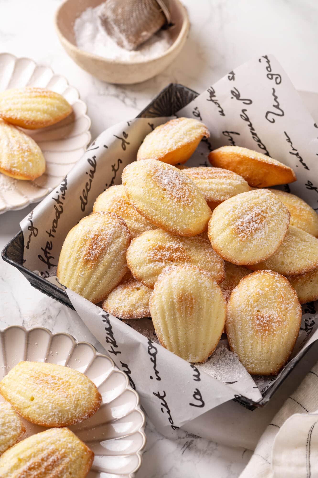 Madeleines in a square bowl with powdered sugar sprinkled on top.