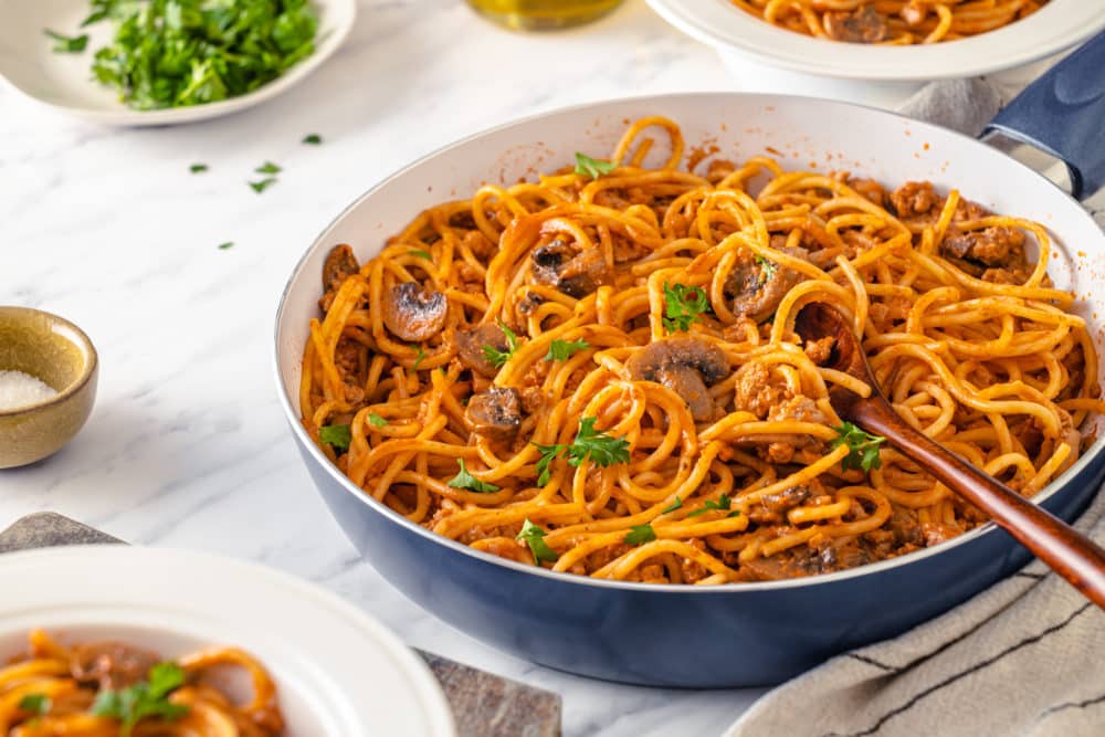 beef-spaghetti-in-a-skillet-with-a-wooden-spoon-with-a-towel-on-the-side