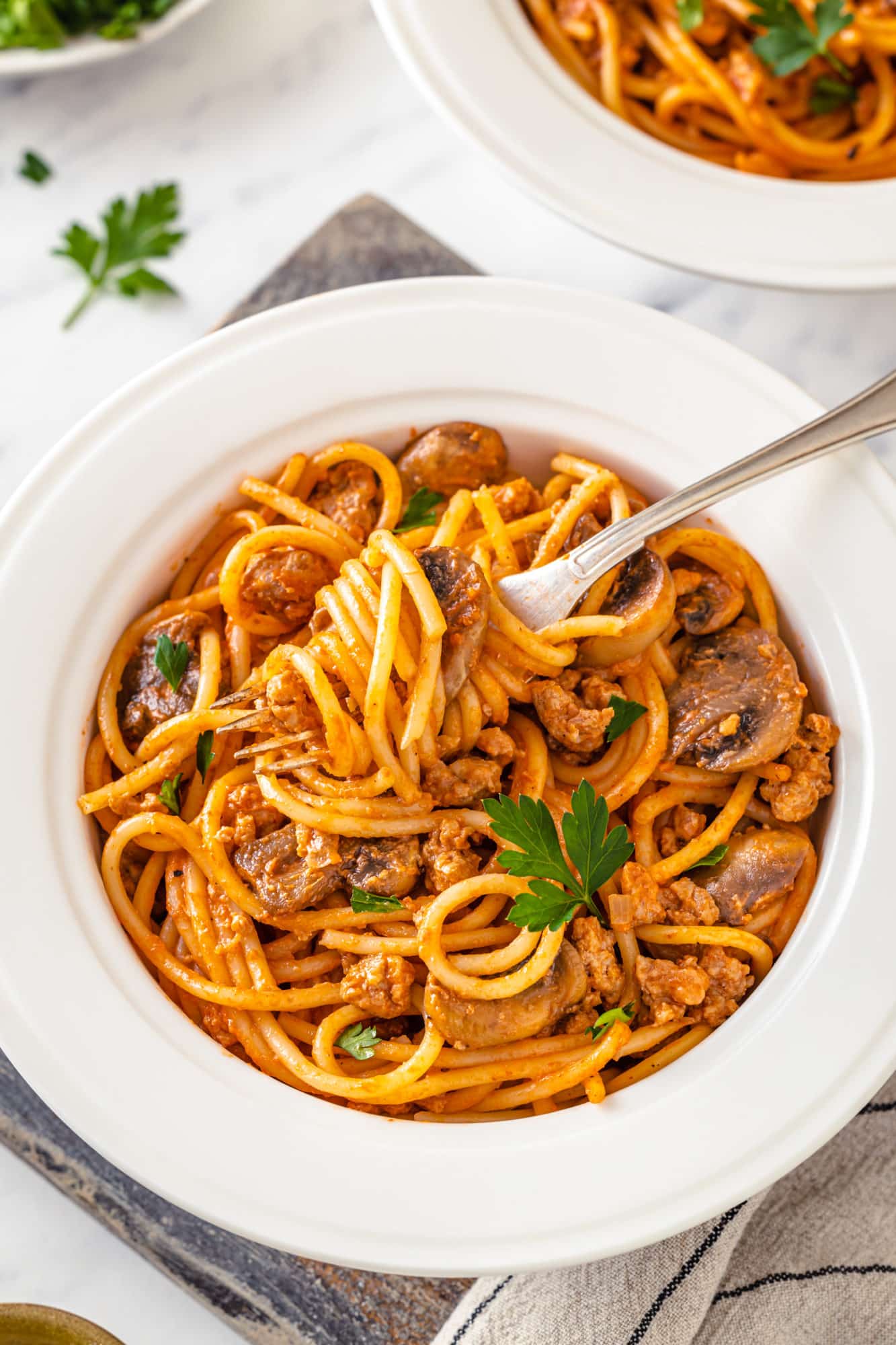 spaghetti with beef and mushrooms in a white bowl with a fork.