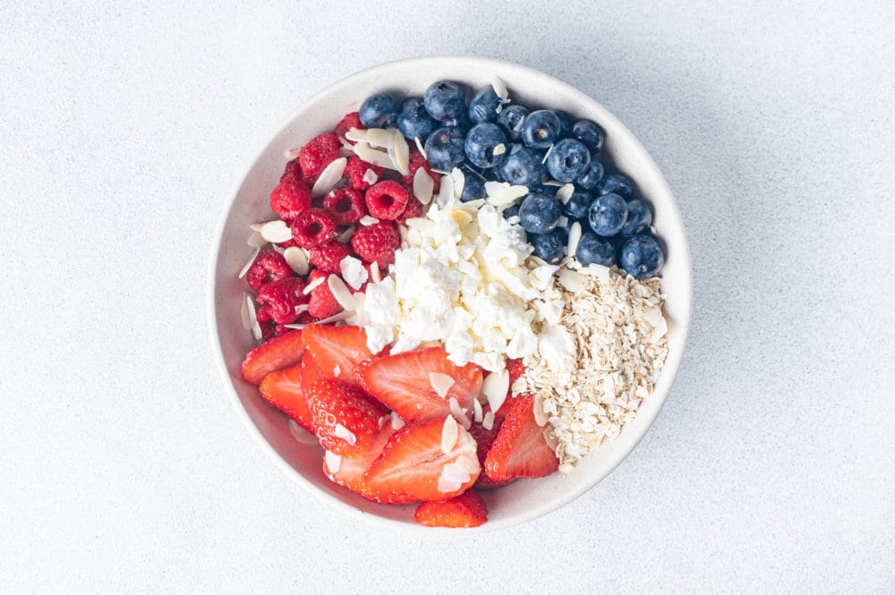 A bowl of cottage cheese, fresh berries, silvered almonds and oats.