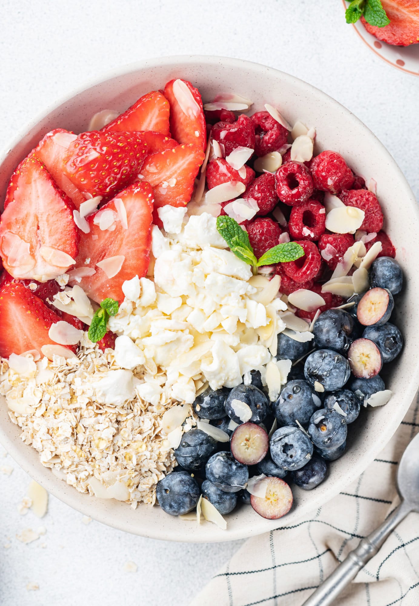 A bowl of cottage cheese and fruit with oats drizzled honey and silvered almonds. 