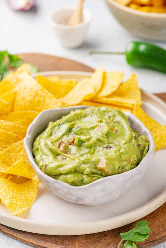 guacamole-in-bowl-with-chips-on-plate-on-wooden-board