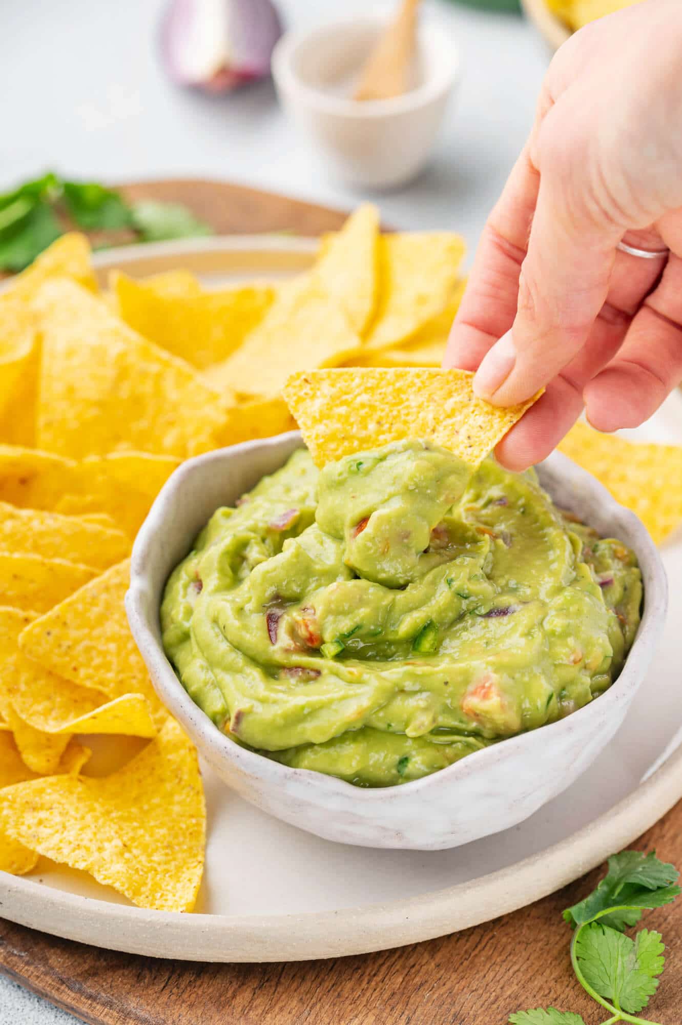 The Best Guacamole Recipe to Serve with Chips guacamole-in-bowl-with-chips-on-plate-hand-scooping-guacamole-with-chip