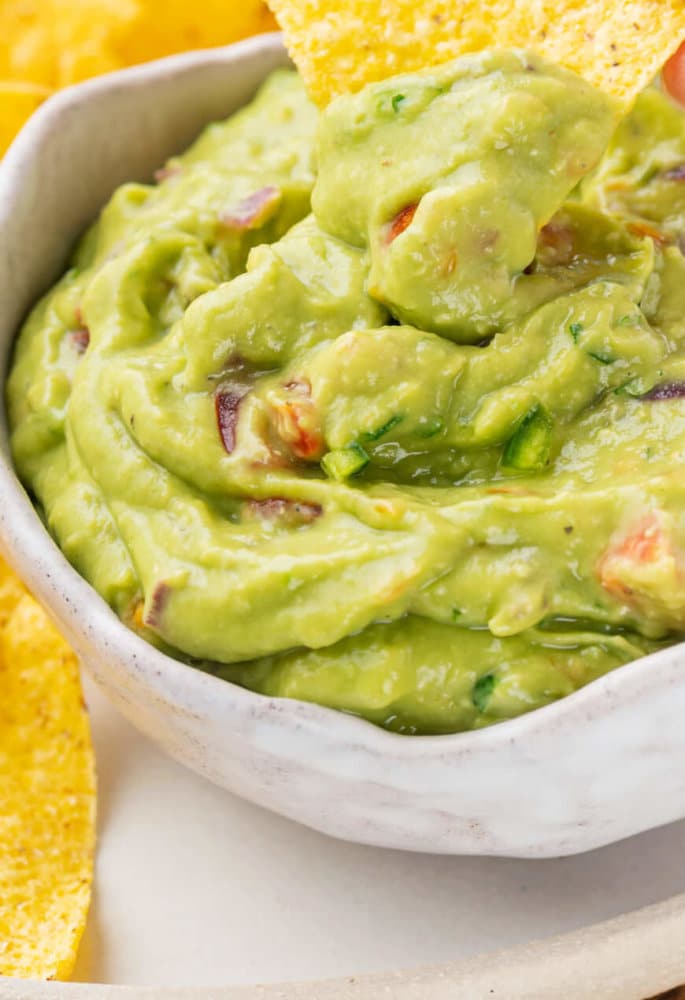 guacamole-in-bowl-with-chips-on-plate-hand-scooping-guacamole-with-chip
