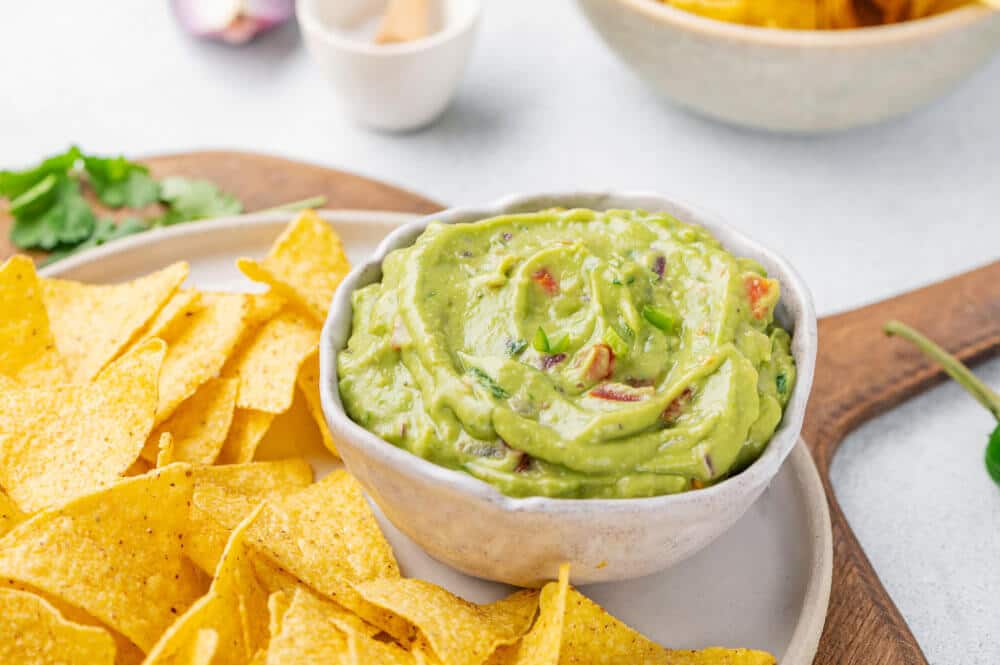 guacamole-in-bowl-with-chips-on-plate-on-wooden-board