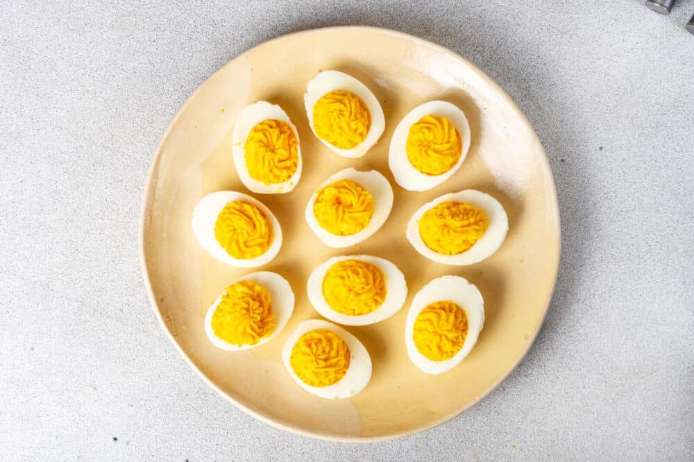 Filled egg whites with egg yolk mixture on a yellow decorative plate.