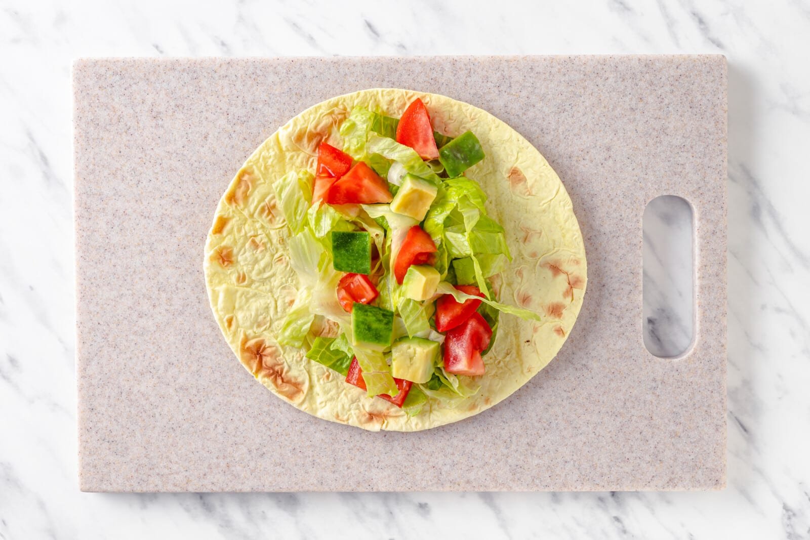 taco being put together with avocado tomato and lettuce in a tortilla on a cutting board.