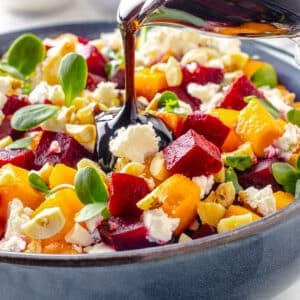 Beet salad in a blue bowl with balsamic dressing being drizzled on top from a glass pitcher.