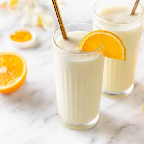 Creamsicle smoothie in a glass with an orange slice on the rim and a straw.