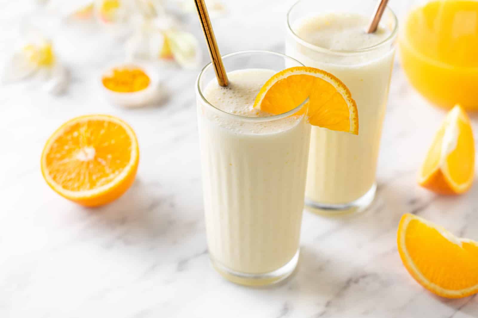 Creamsicle smoothie in a glass with an orange slice on the rim and a straw.