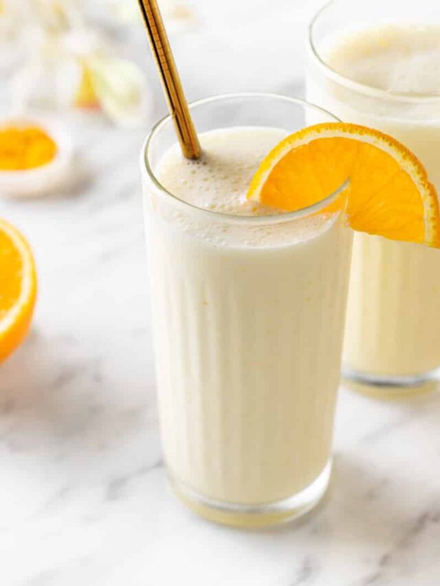 Creamsicle smoothie in a glass with an orange slice on the rim and a straw.