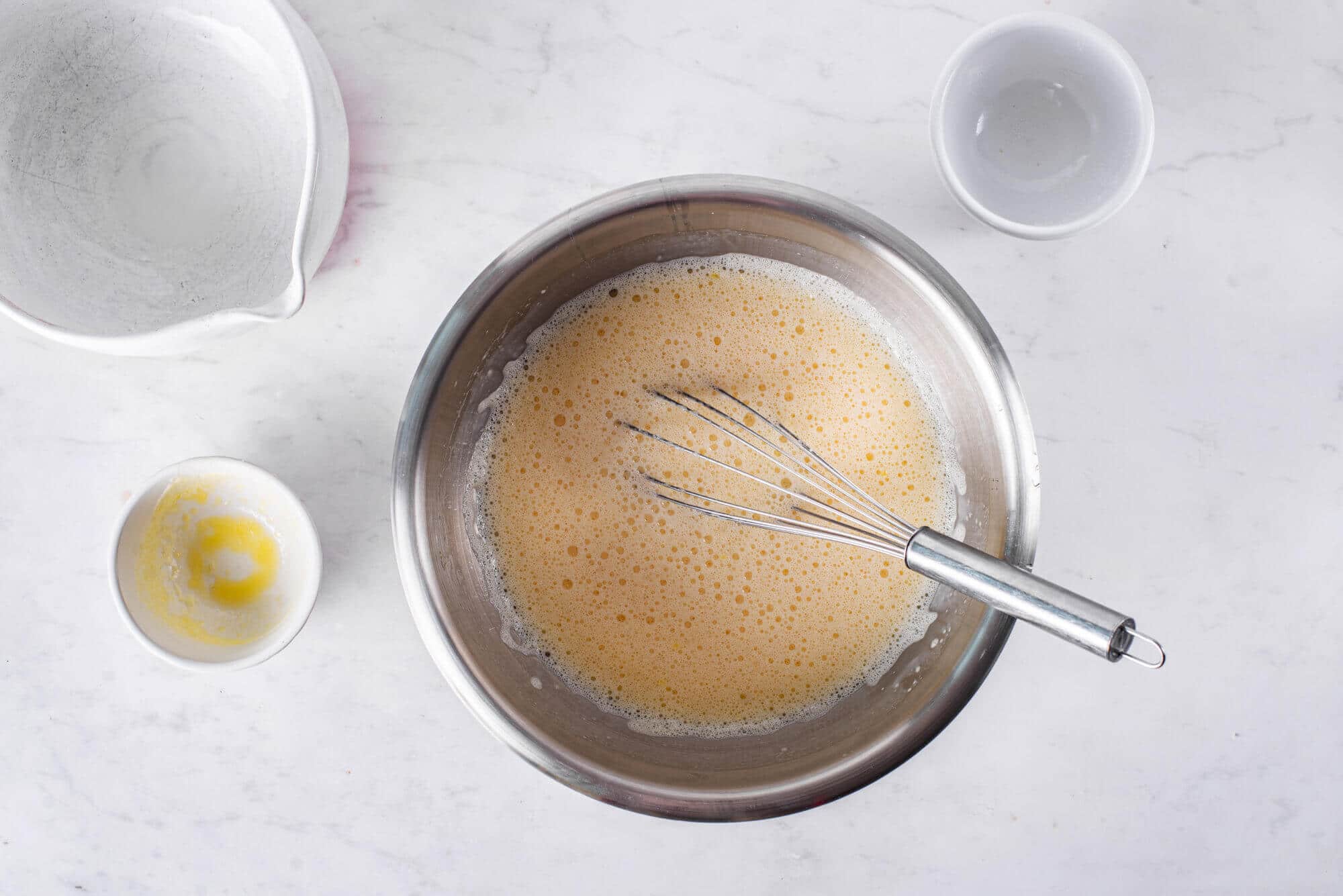 crepes-being-mixed-in-a-silver-bowl-with-a-whisk-and-bowls-on-the-side
