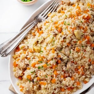 Mound of rice plov on a white plate with forks on the side.