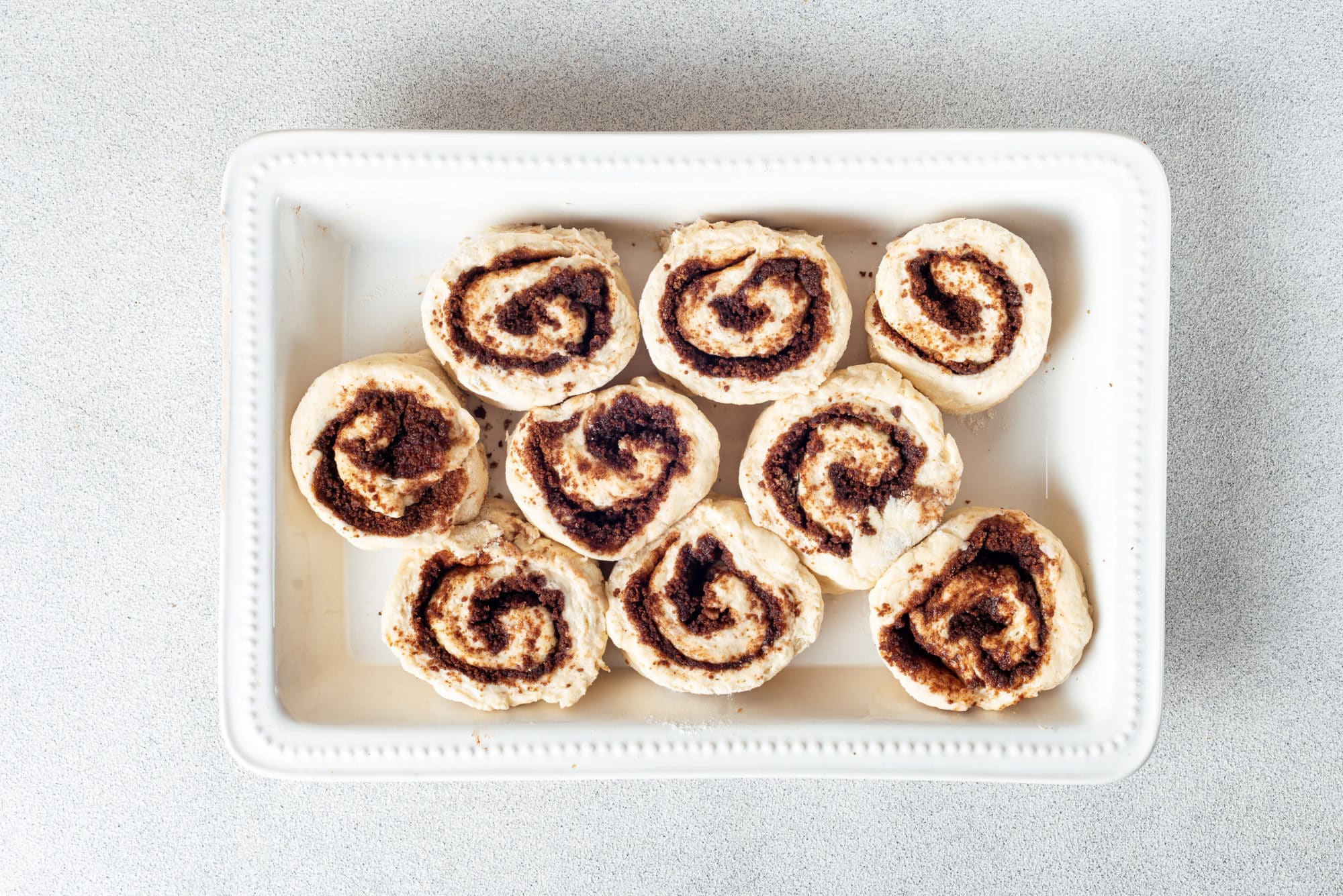 Cinnamon roll dough ready to bake in a white baking tray.