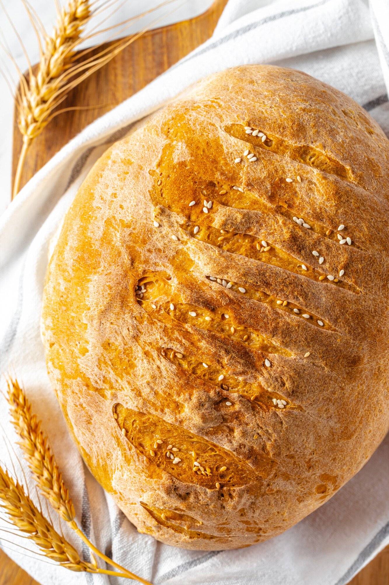 A loaf of bread topped with a sprinkle of sesame seeds on a wooden cutting board.