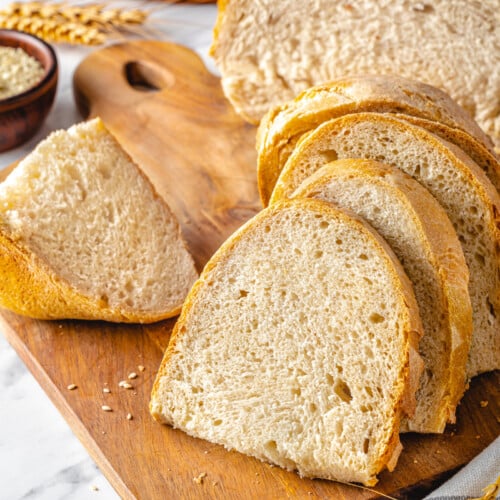 Baked bread slices on a wooden board with a wheat stalk on the side.