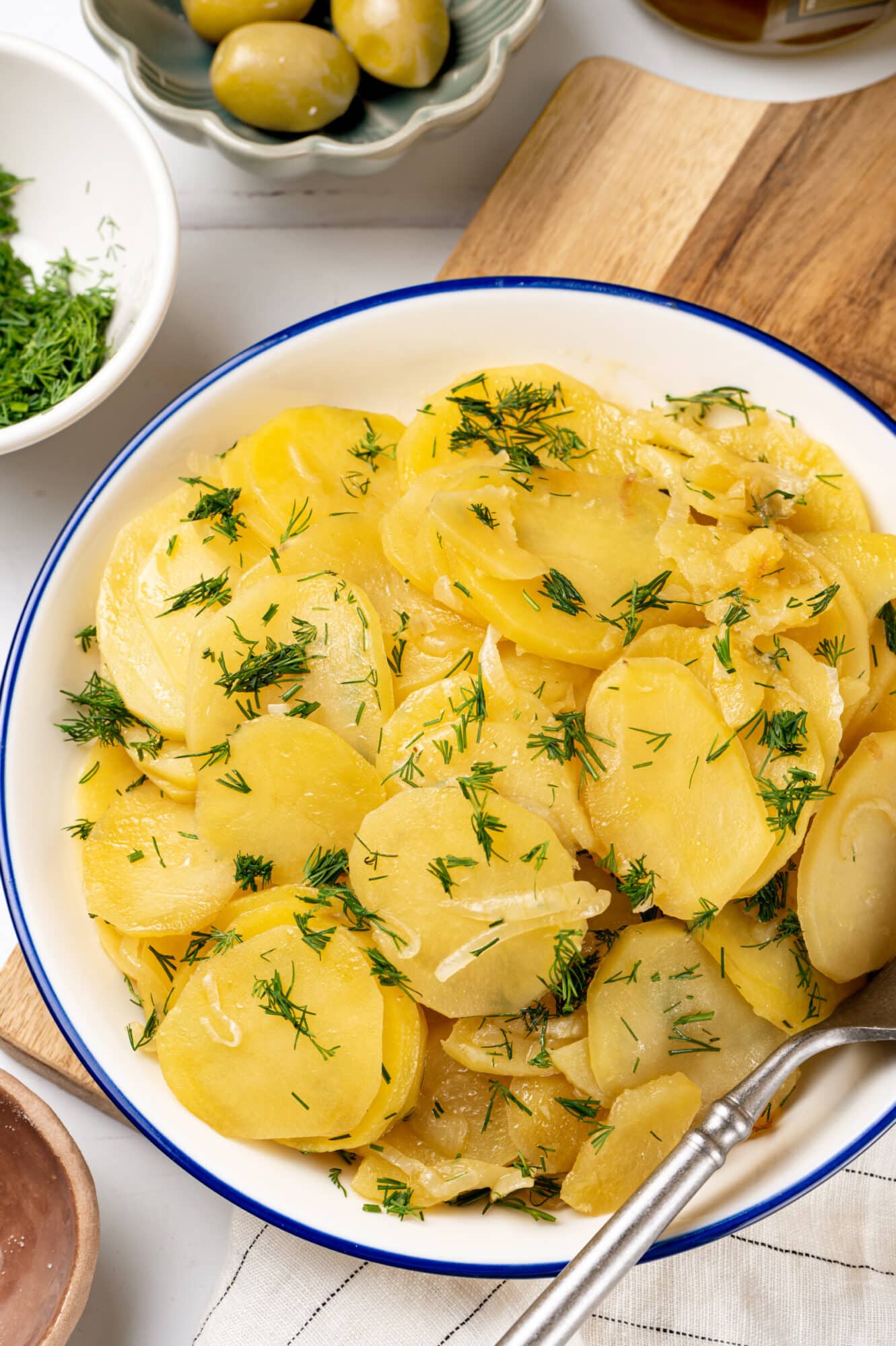 a wooden board with a dish on top with braised potatoes and dill in it.