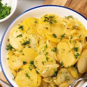 a wooden board with a dish on top with braised potatoes and dill in it.