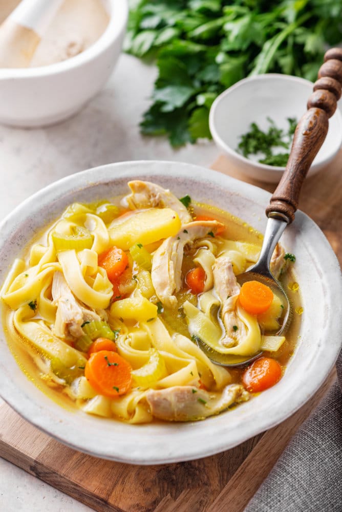 chicken-soup-in-a-white-bowl-on-a-wooden-board-with-a-spoon