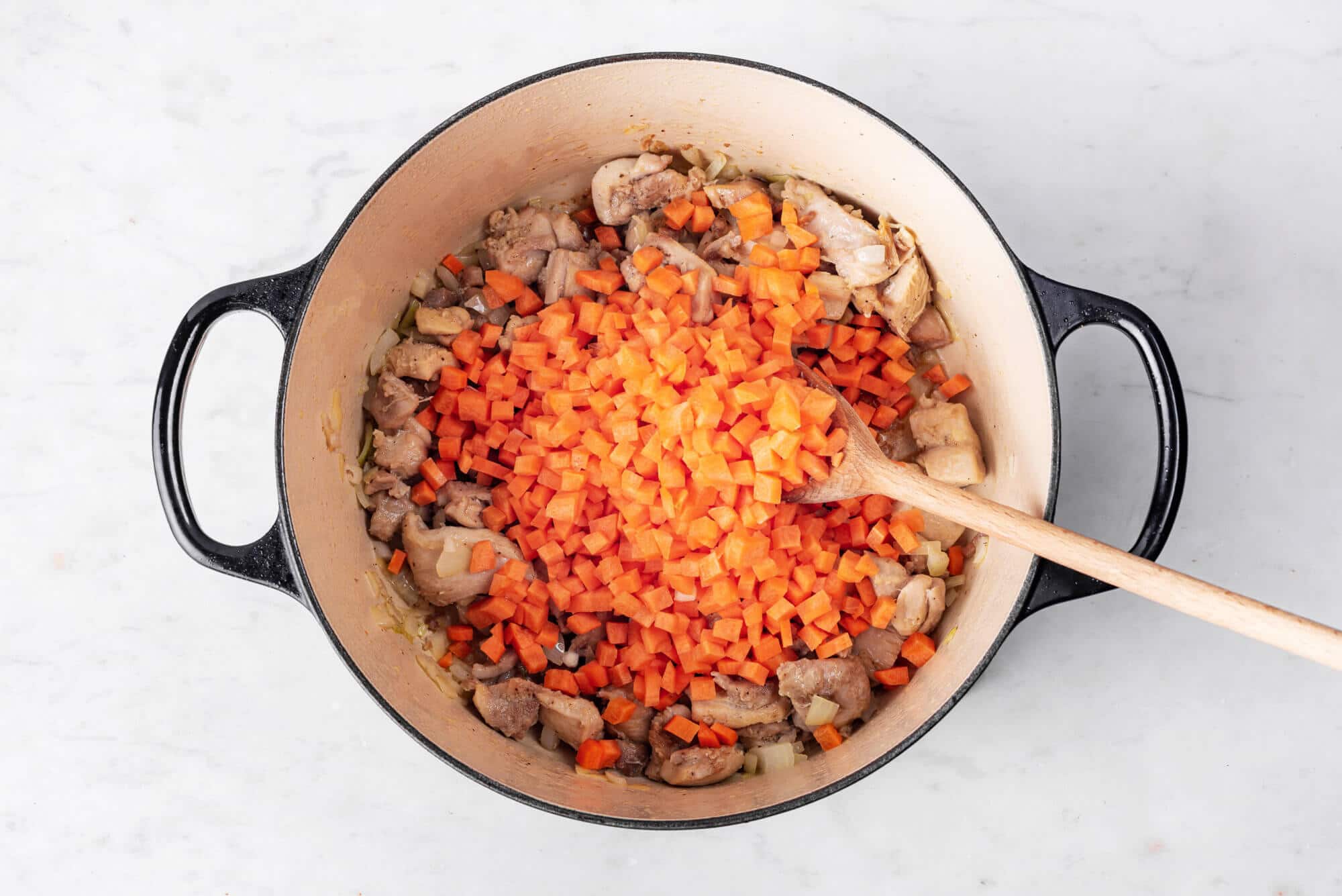 Carrots, chicken, and onion sauteing in a pot.