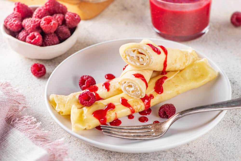 filled-crepes-with-berry-sauce-on-a-white-plate-with-a-fork-and-raspberries