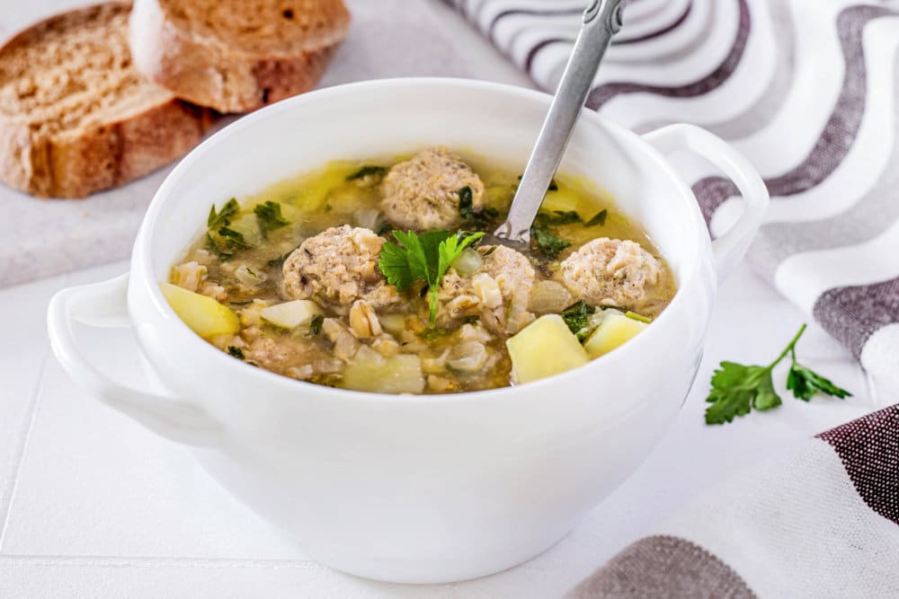 meatball-soup-in-a-white-bowl-with-a-spoon-and-sliced-bread-on-the-side