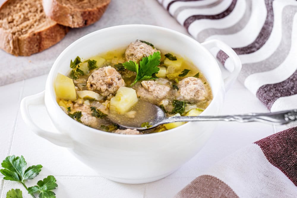 meatball-soup-in-a-white-bowl-with-a-spoon-and-sliced-bread-on-the-side