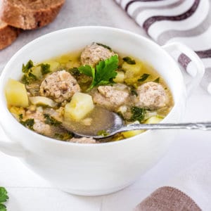 meatball-soup-in-a-white-bowl-with-a-spoon-and-sliced-bread-on-the-side