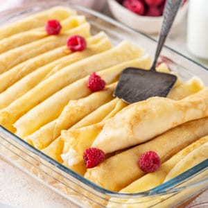 glass baking dish with filled sweet cheese crepes with raspberries with a spatula.