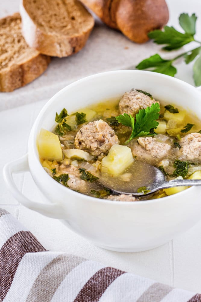 meatball-soup-in-a-white-bowl-with-a-spoon-and-striped-towel-and-sliced-bread