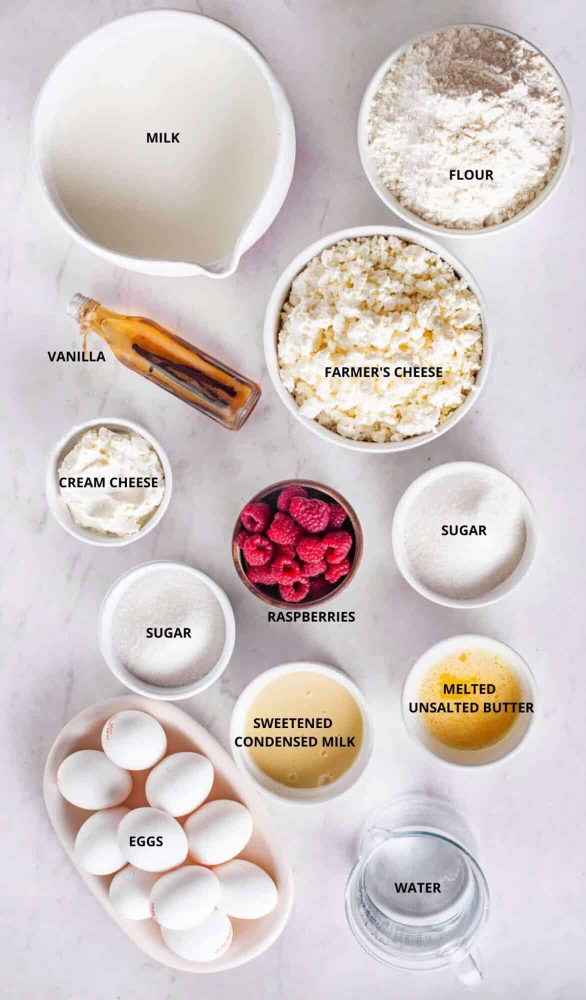 milk in a bowl flour in bowl farmer's cheese in a white bowl bottle of vanilla bowl of cream cheese wooden bowl with raspberries bowl of fine white sugar melted butter bowl of eggs bowl of condensed milk and water.