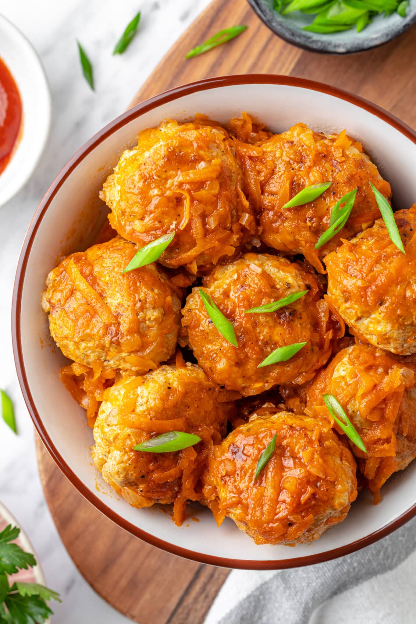 Meatballs garnished with chopped green onion in a bowl.