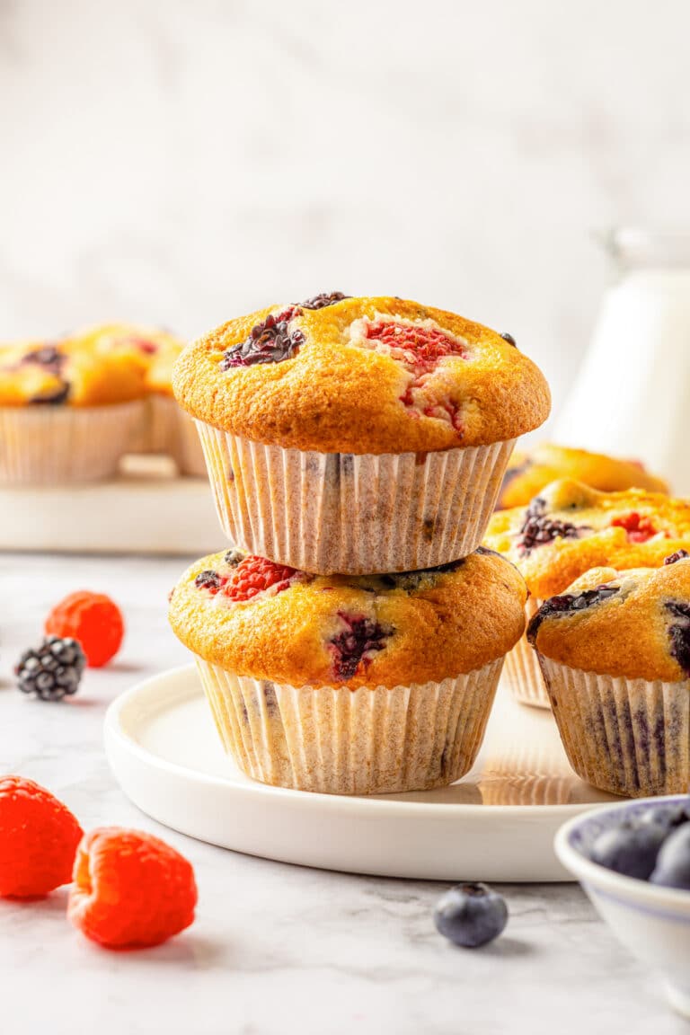 A stack of two no mixer fruit muffins on a white plate surrounded by fresh berries.