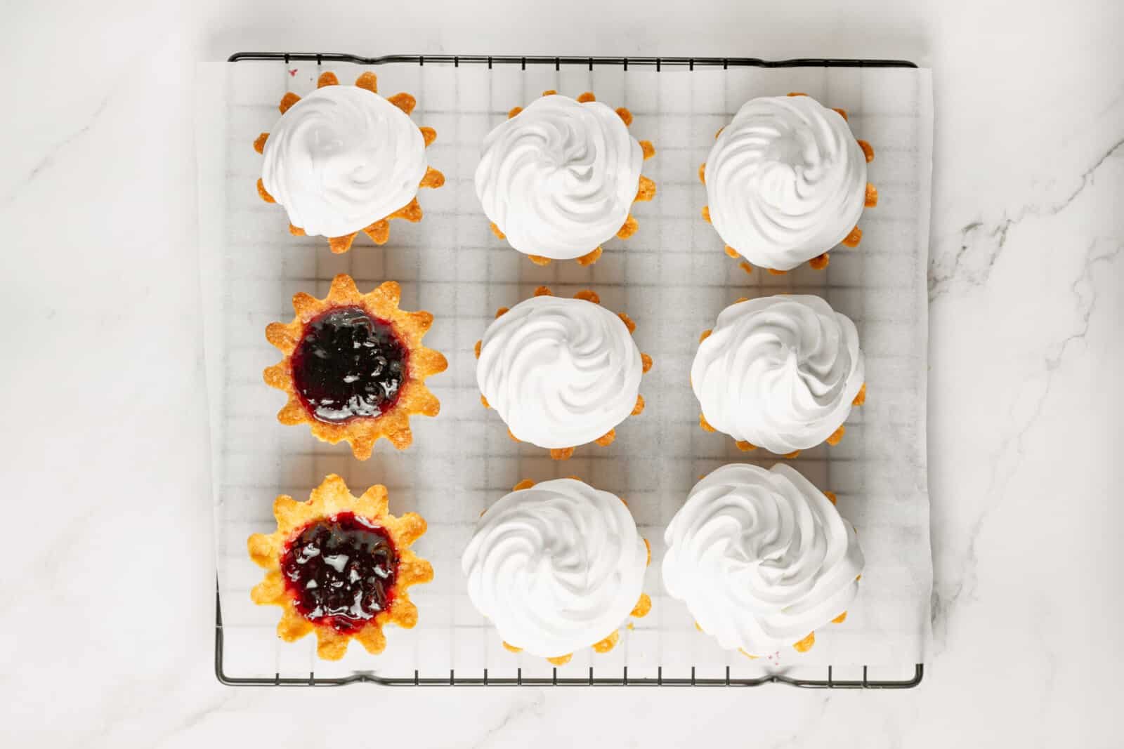 Meringue Jam Filled Tartlets Piping meringue atop tartlets with jam.