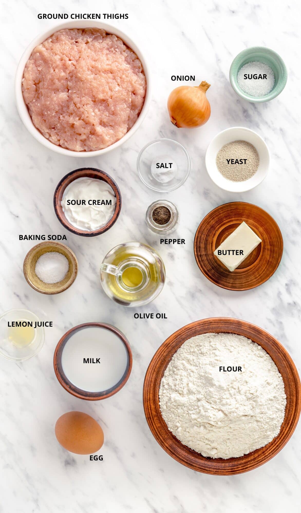 Piroshki ingredients with labels - flour, ground chicken, baking soda, milk, egg, butter, yeast, olive oil, lemon juice, sour cream, pepper, salt, onion, and sugar.