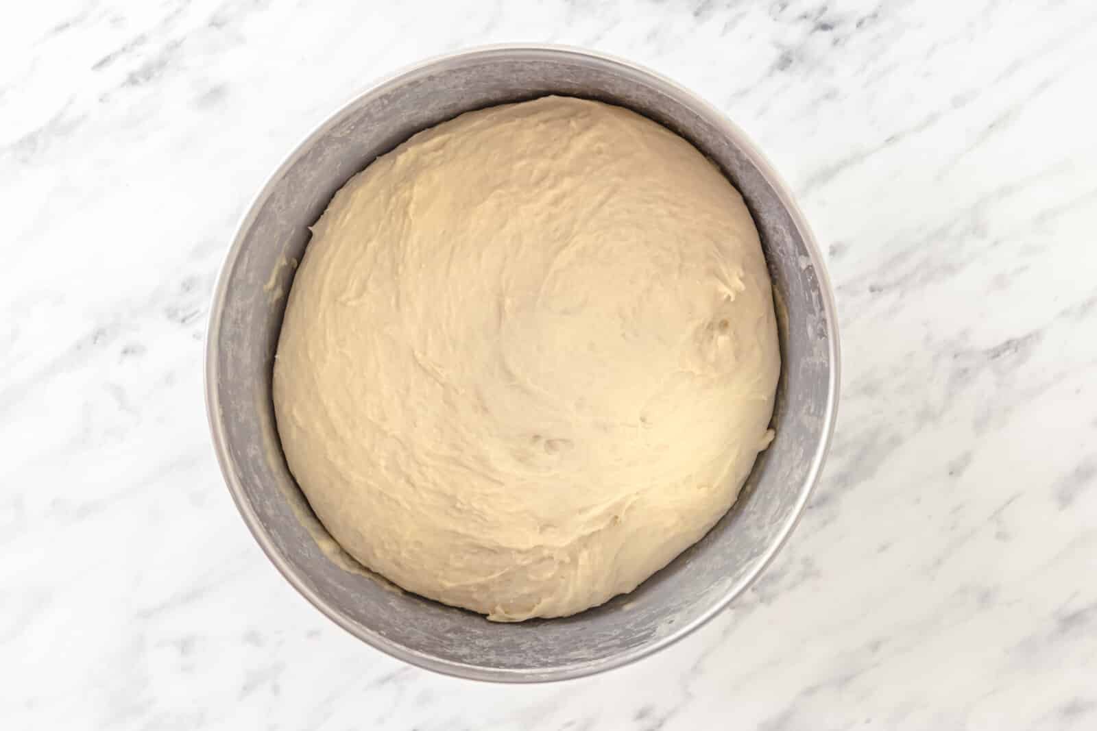 Risen piroshki dough in a silver bowl.