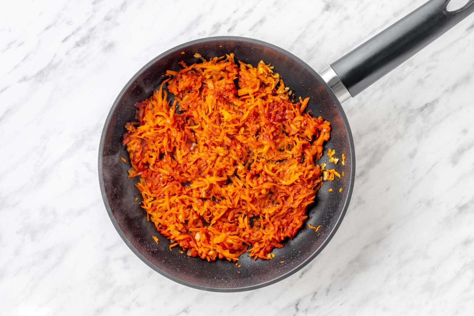 Sautéing carrot and onion in a skillet.