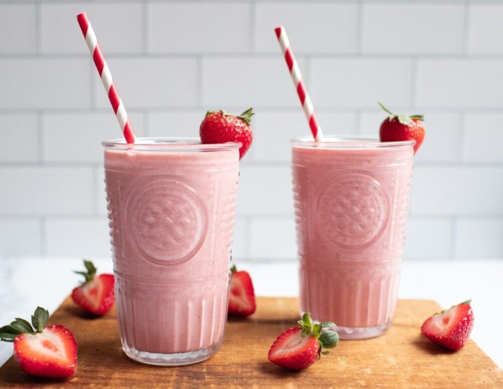 strawberry-banana-smoothie-in-glasses-with-straws-and-strawerries-around-on-a-wooden-board