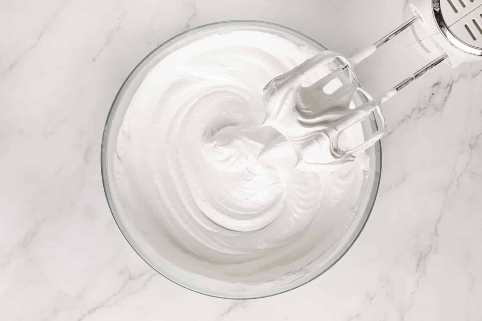 Meringue Jam Filled Tartlets Whipping meringue in a glass bowl with hand mixers.
