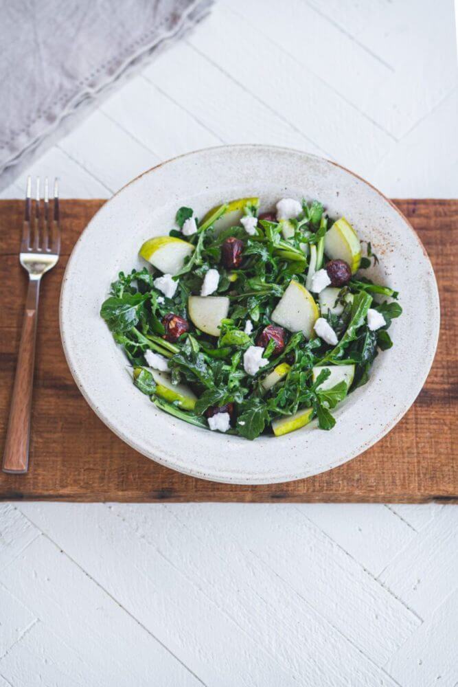 arugula-pear-salad-in-a-white-bowl-on-a-wooden-board-with-a-fork