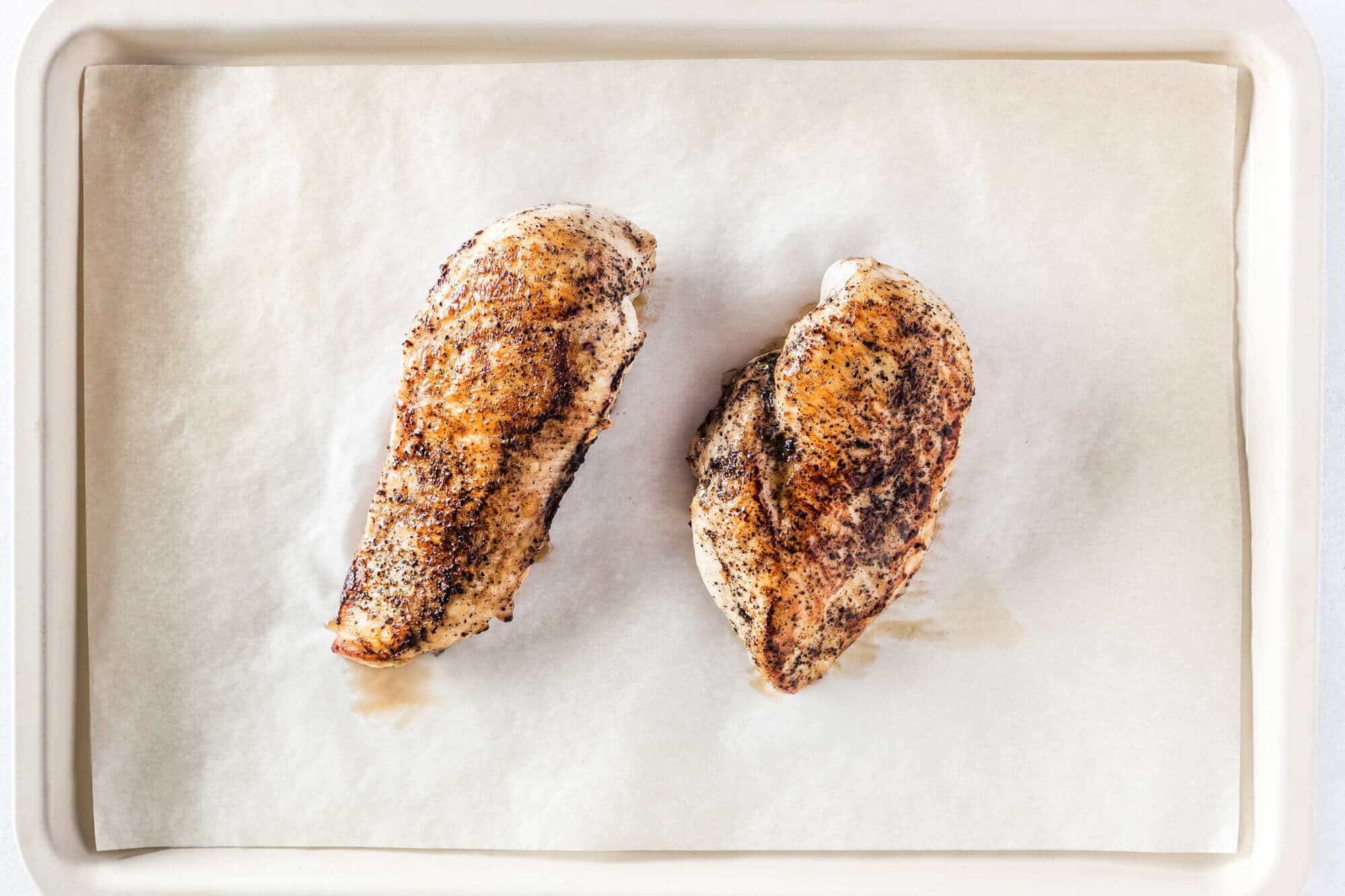 Two cooked chicken breasts on a baking tray with parchment paper.