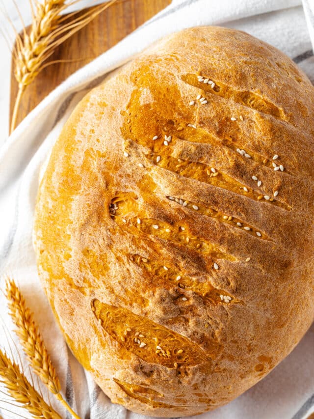 fresh baked bread on a white towel on a wooden board with wheat stalks on the side.