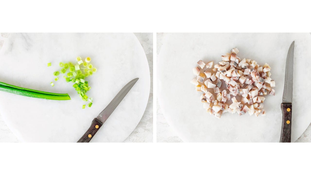 chopped herring on marble board and chopped green onion.