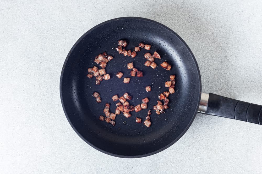 A black skillet with bacon bits cooking.
